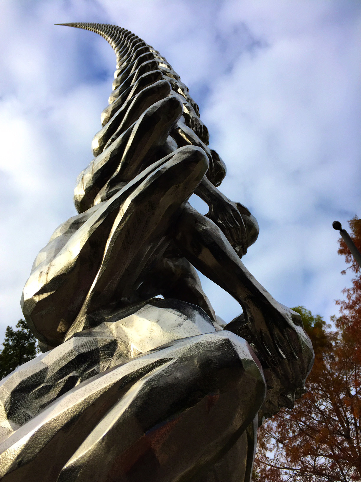 photo of sculpture of spine comprised of people on each other's backs, covering the eyes of the person below.